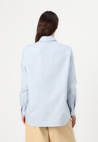 Lys blå skjorte med knapper og lange ermer, klassisk krave og buet kant. Laget av et jevnt stoff med minimal tekstur.