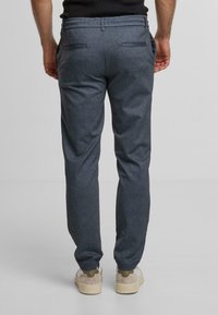 Pantaloni grigi su misura con un motivo sottile, vestibilità slim, tasche laterali e due tasche posteriori. Indossati con sneakers di colore chiaro.