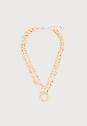 Collana a doppia catena in tono oro con un grande pendente ad anello circolare e dettaglio di chiusura rettangolare su sfondo bianco.