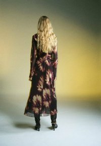 Dlhá, splývavá sukňa s tmavým tie-dye vzorom v purpurových a béžových odtieňoch. Priesvitná látka s dlhými rukávmi, doplnená čiernymi podpätkami.