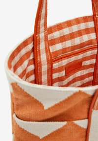 Textil táska narancs és krémszínű geometrikus mintával, kockás belső béléssel, bőr kiegészítőkkel és oldalsó zsebbel.