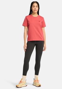 T-shirt corail à manches courtes avec un col rond, associé à des leggings noirs et des chaussures de sport multicolores avec des semelles texturées.