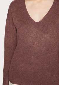 Burgunderröd stickad tröja med djup V-ringning, långa ärmar och en mjuk, texturerad yta. Tyget har en subtil glans.