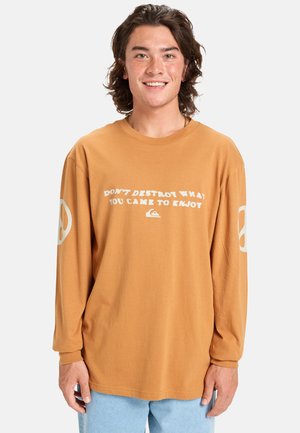Langærmet, sennepsfarvet t-shirt lavet af bomuld med en afslappet pasform. Har hvid tekst og fredssymbol grafik på ærmerne.