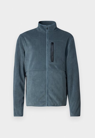 Tumši zilas vilnas jakas, kurai ir augsta apkakle, priekšējais rāvējslēdzējs un krūšu kabata ar melnu akcentu. Gluda, mīksta tekstūra.