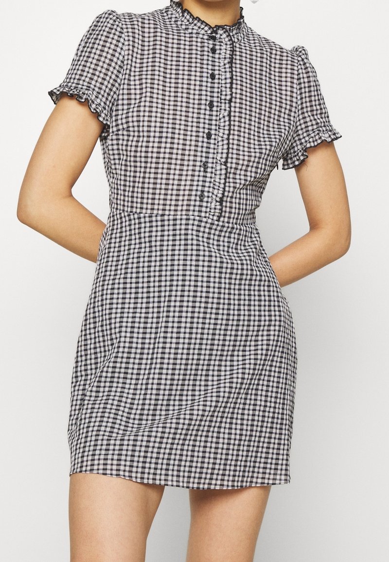 Schwarz-weißer Karo-Kleid mit kurzen Rüschenärmeln, hohem Dekolleté und vorderem Knopfverschluss; tailliert und mit weit auslaufendem Rock.