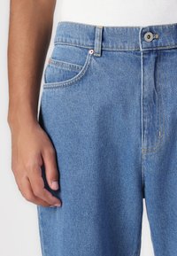 Lyseblå denim jeans med lige snit, der har fem lommer, orange syninger og en metalknaplukning i taljen.