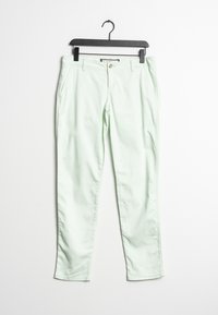 Jasnozielone dopasowane spodnie z zapięciem na guzik i bocznymi kieszeniami wiszące na czarnym wieszaku na białym tle.