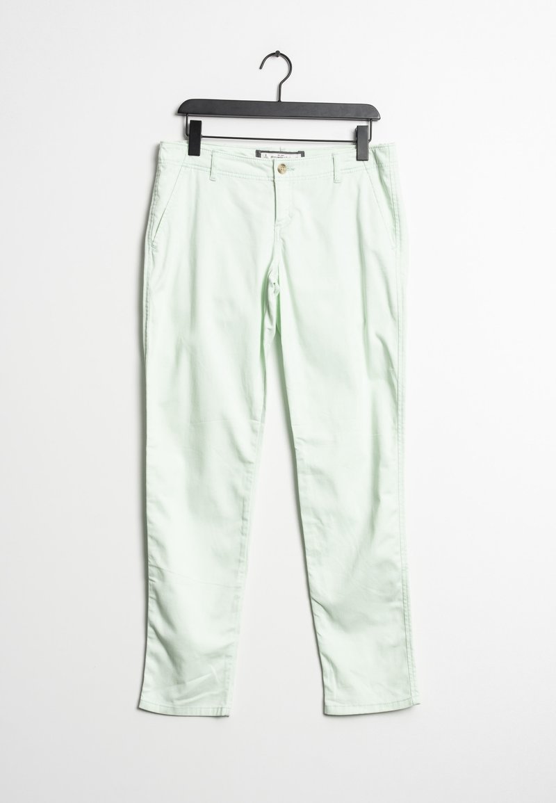 Jasnozielone dopasowane spodnie z zapięciem na guzik i bocznymi kieszeniami wiszące na czarnym wieszaku na białym tle.