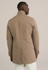 Abrigo beige de longitud media con cuello alto, hecho de un material suave y resistente al agua. Presenta detalles de costura y acentos de botones en los puños.