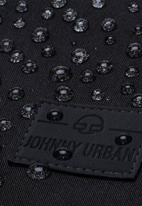 Fekete textúrált felületű szövet, vízcseppekkel. Egy fekete bőr címke van, beütve a "JOHNNY URBAN" felirattal.