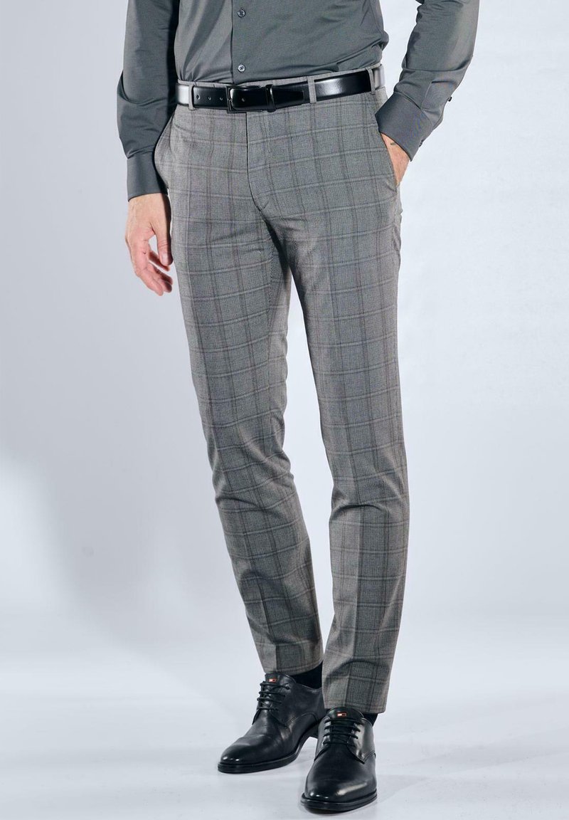 Graue karierte Hose mit schmaler Passform, die eine glatte Textur und Seitentaschen aufweist, kombiniert mit schwarzen Lederschuhen und einem passenden Gürtel.