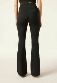 Leggings noires évasées avec taille haute, texture lisse et détails de couture subtils, conçues pour le confort et la flexibilité.