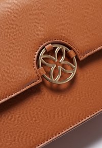 Borsa a mano marrone con texture, dotata di un dettaglio in oro circolare con un design floreale sulla parte anteriore. Forma slim e strutturata.