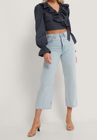 Top corto navy con scollatura arricciata e maniche lunghe a sbuffo, abbinato a jeans a gamba larga blu chiaro e sandali con tacco beige.