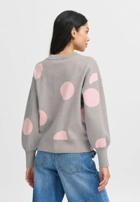 Gray sweater with large pink polka dots, ribbed cuffs, and a crew neckline. Worn with blue high-waisted jeans, showing textured knit detail.