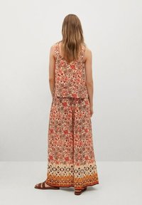 Dwuczęściowy zestaw z kwiatowym wzorem w ciepłych odcieniach. Top bez rękawów o warstwowym wyglądzie oraz spodnie z szerokimi nogawkami i ozdobnym wykończeniem.