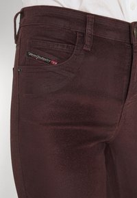 Burgundské džíny s hladkou texturou, přední kapsou s štítkem Diesel Industry a klasickým knoflíkovým zapínáním.