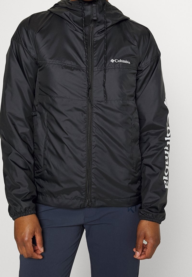 Černá bunda Columbia s kapucí, plným zipem, elastickými manžetami a logem na hrudi a rukávu. Voděodolný materiál s hladkou texturou.