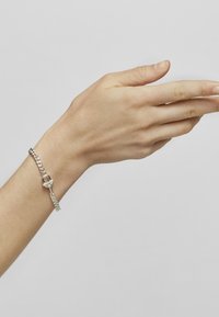 Pulsera de cadena de plata con un cierre redondo, que presenta eslabones entrelazados y un acabado suave y pulido. Mano posicionada para mostrar la pulsera.