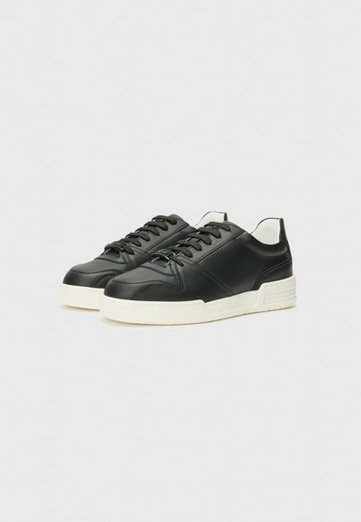 Zwarte leren sneakers met een gladde textuur, witte rubbere zool, ronde neus en traditioneel vetersysteem; minimalistisch ontwerp met contrasterende accenten.