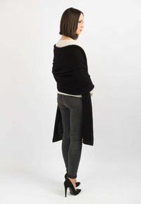 Sort omslagstøj med en tekstureret finish, der draperer sig om kroppen. Båret over en lys top og parret med mørke skinny jeans og sorte hæle.