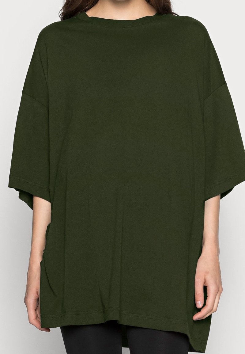 Przestronna, krótko rękawowa koszulka w ciemnozielonym kolorze, wykonana z miękkiej bawełny, z okrągłym dekoltem i bocznymi kieszeniami, o luźnym kroju.