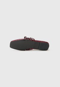 Scarpa slip-on piatta con suola nera e parte superiore in pelle verniciata rossa scura, caratterizzata da più cinturini e una piccola fibbia.