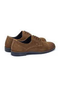 Zapatos de ante marrón con un diseño de perfil bajo, punta redonda y cordones. Presentan costuras en contraste y una suela de goma negra.