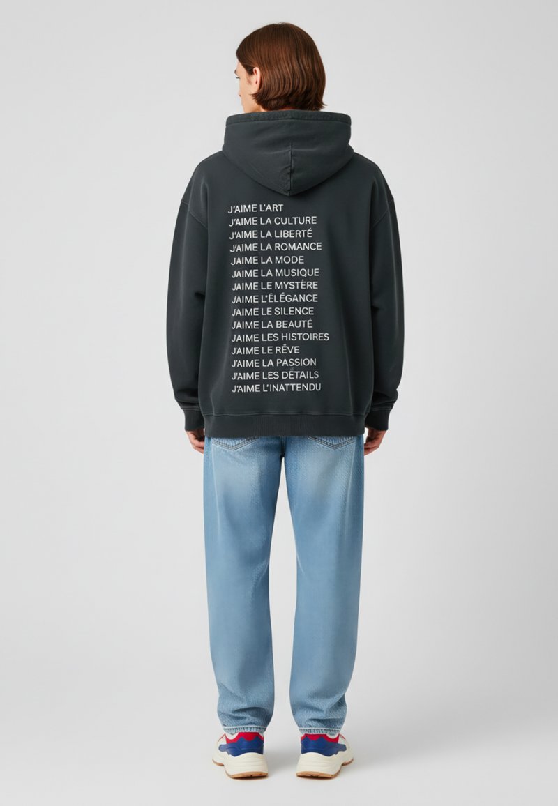 Kolen hoodie met een grote capuchon, met witte verticale tekst op de achterkant. Lichtblauwe spijkerbroek met een relaxed fit en subtiele textuur.