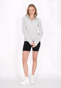 Lys grå zip-up pullover med lange ærmer og krave, parret med sorte shorts og hvide sneakers; glat tekstur, afslappet pasform.