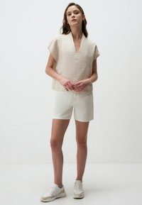 Beige linnen T-shirt met korte mouwen en een V-hals, gecombineerd met lichtcrème shorts. Gecompleteerd met witte sneakers met beige accenten.
