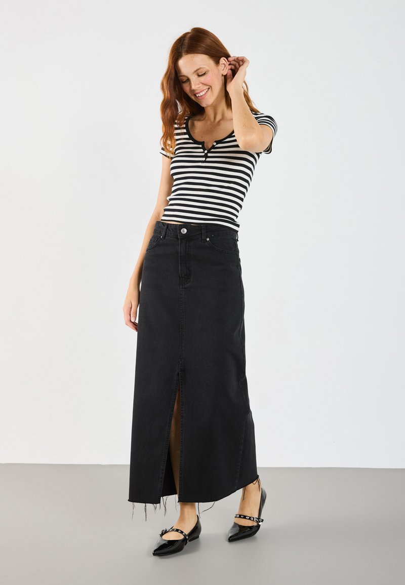 Jupe maxi en denim noir avec une fente à l'avant, taille haute et ourlet effiloché ; associée à un haut à manches courtes noir et blanc à rayures.