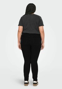 Svarta högmidjade skinny jeans med bakfickor och en slät textur. I kombination med en åtsittande mörkgrå t-shirt och avslappnade vita sneakers.