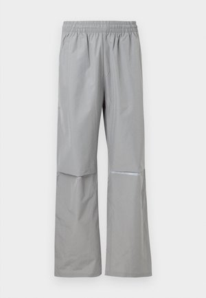 Hellgraue wasserdichte Regenhose mit elastischem Bund und reflektierendem Streifen am rechten Bein, für den Außeneinsatz konzipiert.