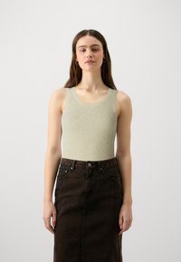 Φωτεινό πράσινο ριγέ αμάνικο μπλουζάκι συνδυασμένο με σκούρα καφέ τζιν φούστα. Το μπλουζάκι έχει στρογγυλή λαιμόκοψη και φαρδιές τιράντες.