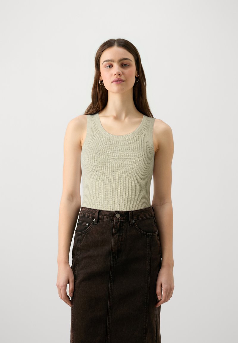 Φωτεινό πράσινο ριγέ αμάνικο μπλουζάκι συνδυασμένο με σκούρα καφέ τζιν φούστα. Το μπλουζάκι έχει στρογγυλή λαιμόκοψη και φαρδιές τιράντες.