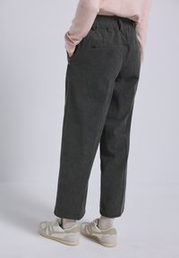 Pantaloni in corduroy grigio scuro con elastico in vita, dotati di tasche laterali e una vestibilità rilassata. Indossati con scarpe da ginnastica di colore chiaro.