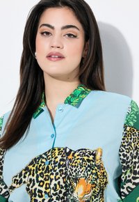 Světle modrá košile na knoflíky s velkým leopardím vzorem, zelené palmové listy jako akcenty na rukávech a límci. Texturovaná látka.