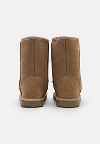 Bottes chelsea en suède brun avec une finition lisse, un design arrondi et des semelles en caoutchouc robustes. Couture détaillée le long des coutures.