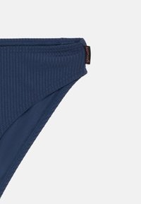 Ναυτικό μπλε ριγωτό bikini κάτω μέρος με καμπυλωτό σχήμα, που διαθέτει ραμμένο λάστιχο στη μέση και μια μικρή επώνυμη ετικέτα στο πλάι.