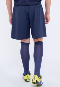Pantalones cortos deportivos de color navy con cinturilla elástica, calcetas hasta la rodilla de color navy y zapatos de fútbol con acentos amarillos que presentan detalles en negro y azul.