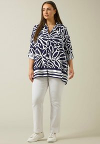 Navy en witte gestreepte shirt met botanisch ontwerp, lange mouwen opgerold, gecombineerd met witte rechttoe rechtaan broek en witte sneakers.