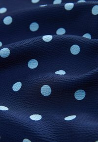 Tissu bleu foncé texturé avec des pois bleu clair espacés régulièrement et de doux plis créant des ombres douces.