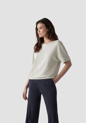 Light grey short-sleeve top with a round neckline, smooth texture, and relaxed fit, worn with dark navy wide-leg pants.