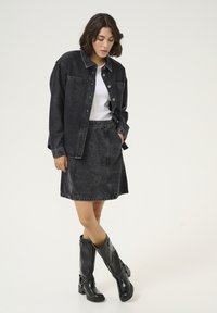 Compleu format din jachetă și fustă din denim negru, cu o cămașă albă dedesubt. Botine negre până la genunchi, cu detalii cu cataramă. Design simplu, ajustat.
