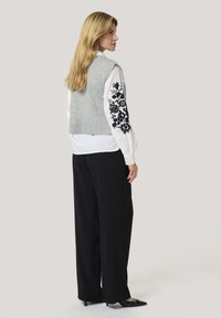 Gray knitted vest, white blouse with black floral embroidery on sleeves, black wide-leg pants, and black shoes. Back view.