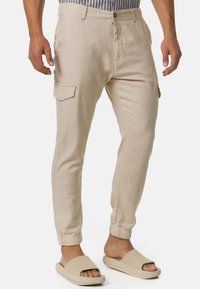 Helle beige Cargo-Hosen aus Leinenmischung mit elastischen Bündchen, Seitentaschen und einem lockeren Schnitt. Kombiniert mit beigen Slip-On-Sandalen.