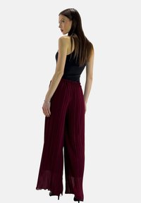 Pantaloni ampi a pieghe in bordeaux con un elastico in vita e tessuto fluido. Indossati con una maglietta nera aderente, che mette in risalto una silhouette rilassata.
