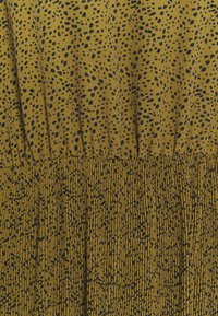 Tissu jaune avec un motif moucheté noir. La partie supérieure est lisse, se transformant en une section plissée en bas. Texture douce partout.